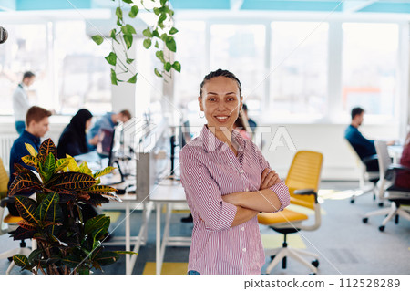 Portrait of young smiling business woman in creative open space coworking startup office. Successful businesswoman standing in office with copyspace. Coworkers working in background 112528289