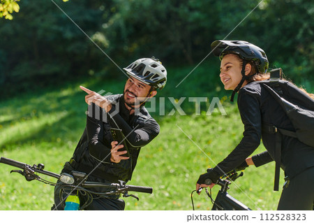A sweet couple, equipped with bicycles and engrossed in coordinating their journey, checks their GPS mobile and watches while planning scenic routes in the park, seamlessly blending technology and A sweet couple, equipped with bicycles and engrossed in coordinating their journey, checks their GPS mobile and watches while planning scenic routes in the park, seamlessly blending technology and 112528323