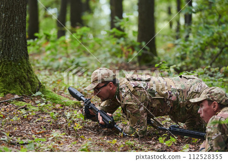 Elite soldiers stealthily maneuver through the dense forest, camouflaged in specialized gear, as they embark on a covert and strategic military mission 112528355
