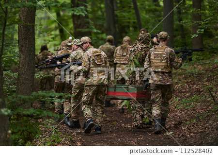 Elite military unit, cloaked in camouflage, transports a crate of ammunition through the dense forest, epitomizing strategic readiness and precision in their covert mission 112528402
