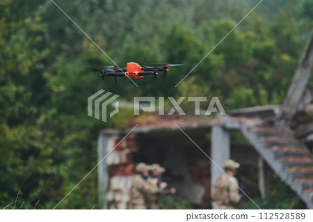 Elite military unit, equipped with state-of-the-art technology including a drone, strategically navigates and surveys dangerous wooded terrain, showcasing their precision, cooperation, and specialized Elite military unit, equipped with state-of-the-art technology including a drone, strategically navigates and surveys dangerous wooded terrain, showcasing their precision, cooperation, and specialized 112528589