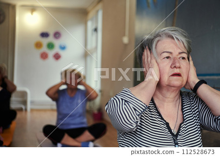 A group of senior women engage in various yoga exercises, including neck, back, and leg stretches, under the guidance of a trainer in a sunlit space, promoting well-being and harmony A group of senior women engage in various yoga exercises, including neck, back, and leg stretches, under the guidance of a trainer in a sunlit space, promoting well-being and harmony 112528673