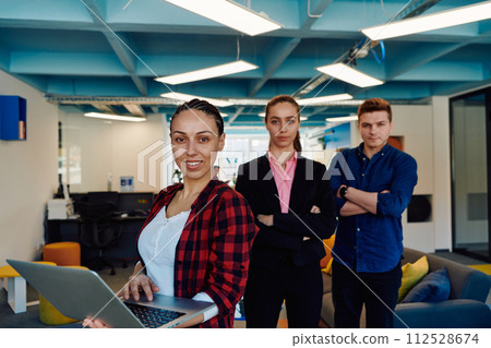 A young team of business professionals poses for a startup office portrait, exuding confidence and ambition, with one woman holding a laptop, symbolizing innovation and collaboration in A young team of business professionals poses for a startup office portrait, exuding confidence and ambition, with one woman holding a laptop, symbolizing innovation and collaboration in 112528674