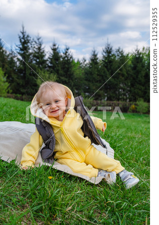 In a spring park, a smiling baby boy is sitting on a blanket on a blanket 112529355