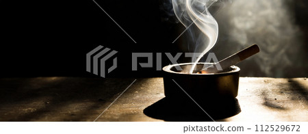 木桌上的煙灰缸裡放著一根點燃的香菸 112529672