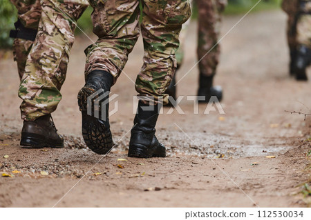 Close up photo, the resilient legs of elite soldiers, clad in camouflage boots, stride purposefully along a hazardous forest path as they embark on a high-stakes military mission Close up photo, the resilient legs of elite soldiers, clad in camouflage boots, stride purposefully along a hazardous forest path as they embark on a high-stakes military mission 112530034
