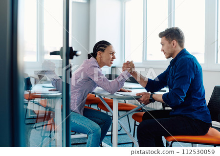 In a modern startup office, a businessman and a businesswoman business colleagues engage in a symbolic arm-wrestling match, reflecting teamwork, competition, and innovation in their dynamic workplace. In a modern startup office, a businessman and a businesswoman business colleagues engage in a symbolic arm-wrestling match, reflecting teamwork, competition, and innovation in their dynamic workplace. 112530059