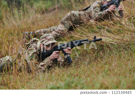 Elite soldiers stealthily maneuver through the dense forest, camouflaged in specialized gear, as they embark on a covert and strategic military mission Elite soldiers stealthily maneuver through the dense forest, camouflaged in specialized gear, as they embark on a covert and strategic military mission 112530485