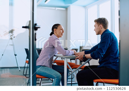 In a modern startup office, a businessman and a businesswoman business colleagues engage in a symbolic arm-wrestling match, reflecting teamwork, competition, and innovation in their dynamic workplace. In a modern startup office, a businessman and a businesswoman business colleagues engage in a symbolic arm-wrestling match, reflecting teamwork, competition, and innovation in their dynamic workplace. 112530626