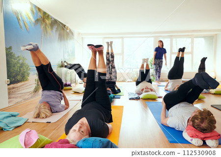 A group of senior women engage in various yoga exercises, including neck, back, and leg stretches, under the guidance of a trainer in a sunlit space, promoting well-being and harmony A group of senior women engage in various yoga exercises, including neck, back, and leg stretches, under the guidance of a trainer in a sunlit space, promoting well-being and harmony 112530908