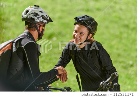 A sweet couple, equipped with bicycles and engrossed in coordinating their journey, checks their GPS mobile and watches while planning scenic routes in the park, seamlessly blending technology and 112531171