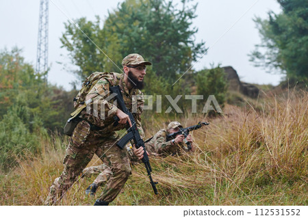 Elite soldiers stealthily maneuver through the dense forest, camouflaged in specialized gear, as they embark on a covert and strategic military mission Elite soldiers stealthily maneuver through the dense forest, camouflaged in specialized gear, as they embark on a covert and strategic military mission 112531552