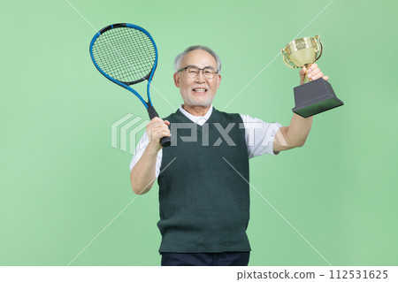 A senior man with a tennis racket and a trophy 112531625