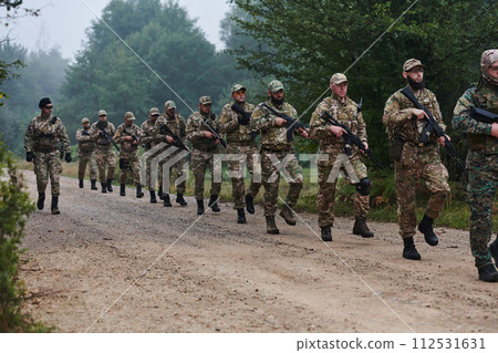 An elite military unit, led by a major, confidently parades through dense forest, showcasing precision, discipline, and readiness for high-risk operations An elite military unit, led by a major, confidently parades through dense forest, showcasing precision, discipline, and readiness for high-risk operations 112531631