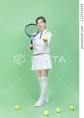 A senior woman holding a tennis racket and a tennis ball 112531648