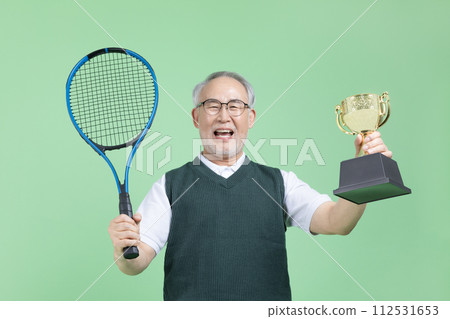 A senior man with a tennis racket and a trophy 112531653