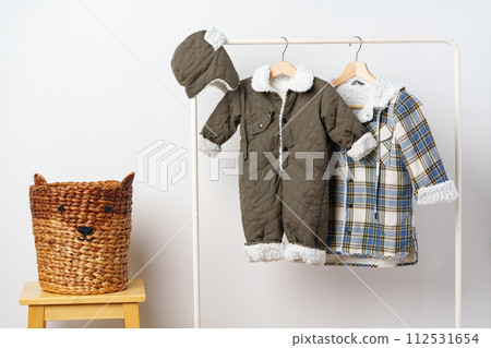 Two kids winter coats hanging on hangers against white wall 112531654