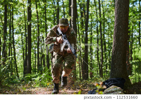An elite soldier, camouflaged and stealthily navigating through dangerous woodland terrain, executes a covert mission in a secluded forest area 112531660