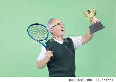 A senior man with a tennis racket and a trophy 112531664