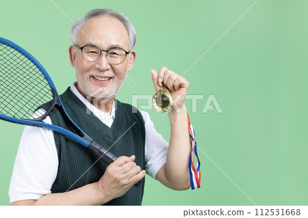 A senior male holding a tennis racket and a medal 112531668