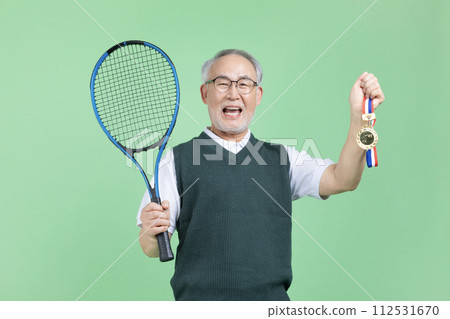 A senior male holding a tennis racket and a medal A senior male holding a tennis racket and a medal 112531670