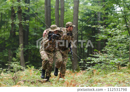 Elite soldier displays unwavering camaraderie and compassion as he aids his injured comrade, skillfully extracting him from the forest with a stretcher, showcasing the profound bond and selflessness 112531798