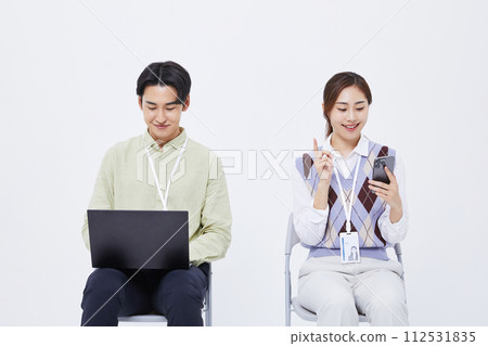 A man and a woman sitting in a chair playing a laptop and a smartphone 112531835