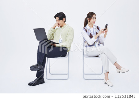 A man and a woman sitting in a chair playing a laptop and a smartphone A man and a woman sitting in a chair playing a laptop and a smartphone 112531845