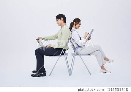 A man and a woman sitting back to back and playing a tablet with a laptop 112531848
