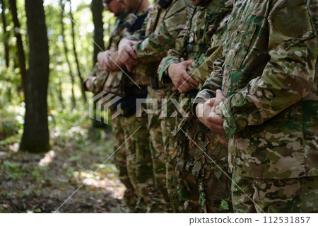 A dedicated group of soldiers engages in Islamic prayer amidst the challenging and perilous conditions of a military operation in dense forested areas 112531857