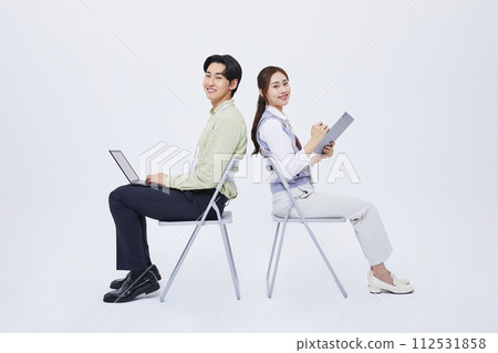 A man and a woman sitting back to back and playing a tablet with a laptop 112531858