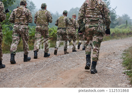 An elite military unit, led by a major, confidently parades through dense forest, showcasing precision, discipline, and readiness for high-risk operations An elite military unit, led by a major, confidently parades through dense forest, showcasing precision, discipline, and readiness for high-risk operations 112531868