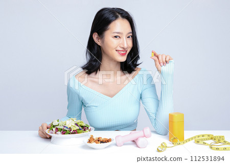 A woman holding a pill in front of her diet and exercise equipment A woman holding a pill in front of her diet and exercise equipment 112531894
