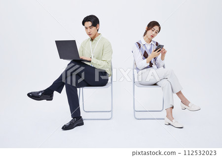 A man and a woman sitting in a chair playing a laptop and a smartphone 112532023