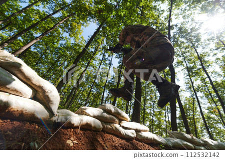 An elite soldier adeptly clears military barriers in the perilous wooded terrain, showcasing tactical skill and agility during specialized training An elite soldier adeptly clears military barriers in the perilous wooded terrain, showcasing tactical skill and agility during specialized training 112532142