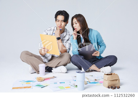 A man and a woman sitting on two legs and holding a tablet and talking 112532260