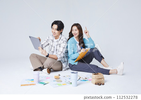 A man and a woman sitting on two legs and holding a tablet and talking 112532278