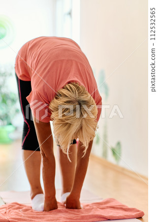 In a sunlit space, a senior woman gracefully practices rejuvenating yoga, focusing on neck, back, and leg stretches, embodying serenity and well-being In a sunlit space, a senior woman gracefully practices rejuvenating yoga, focusing on neck, back, and leg stretches, embodying serenity and well-being 112532565