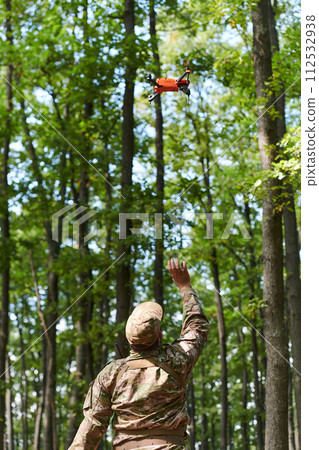 Elite military unit, equipped with state-of-the-art technology including a drone, strategically navigates and surveys dangerous wooded terrain, showcasing their precision, cooperation, and specialized 112532938