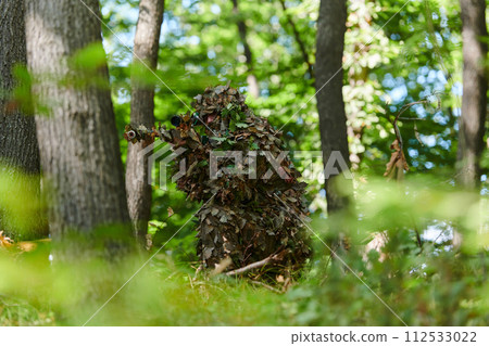 A highly skilled elite sniper, camouflaged in the dense forest, stealthily maneuvers through dangerous woodland terrain on a covert and precise mission 112533022