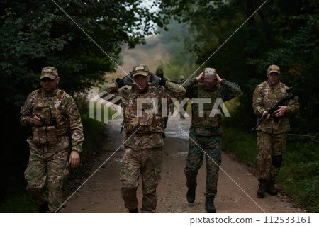 A group of elite soldiers leads captives through a military camp, showcasing a tense atmosphere of detention and security operations A group of elite soldiers leads captives through a military camp, showcasing a tense atmosphere of detention and security operations 112533161