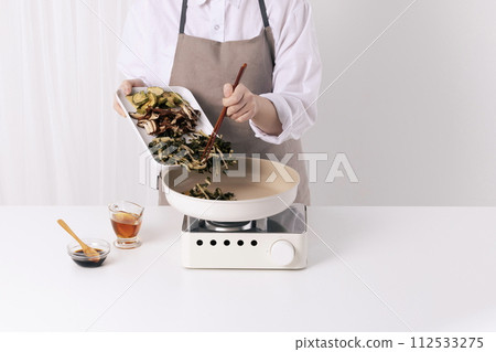 A woman is putting dried Siraegi leaf salad soaked in a frying pan with chopsticks 112533275