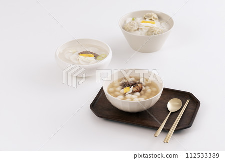 On a white table, three bowls of rice cake soup are placed with kimchi 112533389