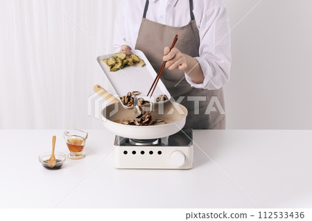 A woman is putting mushrooms soaked in a frying pan with chopsticks 112533436