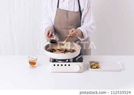 A woman is putting soy sauce in a frying pan with a wooden spoon A woman is putting soy sauce in a frying pan with a wooden spoon 112533524