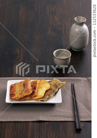 With a wooden table in the background, there's a group pancake, chopsticks, a bottle and a glass With a wooden table in the background, there's a group pancake, chopsticks, a bottle and a glass 112533628