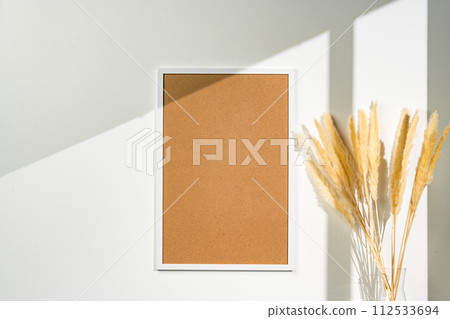 White blank photo frame with dry flowers in vase against white wall 112533694
