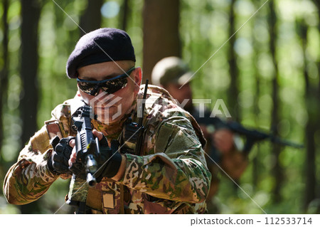 An elite soldier, camouflaged and stealthily navigating through dangerous woodland terrain, executes a covert mission in a secluded forest area An elite soldier, camouflaged and stealthily navigating through dangerous woodland terrain, executes a covert mission in a secluded forest area 112533714