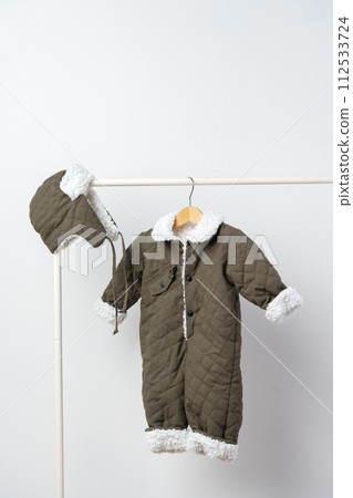 Baby gray quilted winter overalls on hanger against white wall 112533724