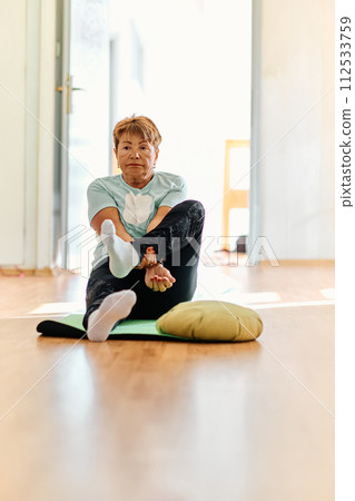 In a sunlit space, a senior woman gracefully practices rejuvenating yoga, focusing on neck, back, and leg stretches, embodying serenity and well-being In a sunlit space, a senior woman gracefully practices rejuvenating yoga, focusing on neck, back, and leg stretches, embodying serenity and well-being 112533759